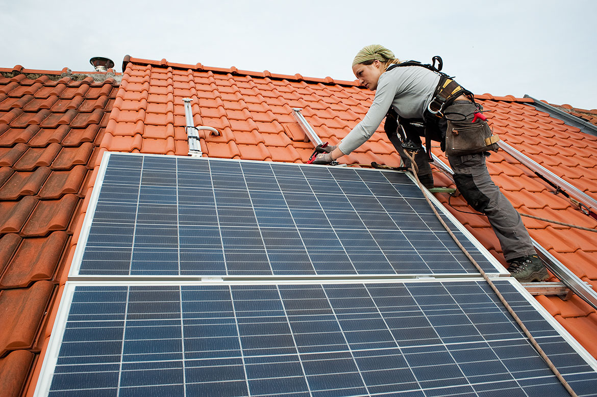Une femme installe des panneaux solaires sur un toit.