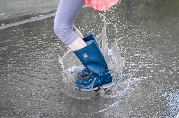 Un enfant avec des bottes saute dans une flaque d'eau dans une rue inondée.