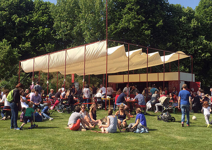 Un parc avec un espace de restauration, des gens assis dans l'herbe ou à table et des gens en balade