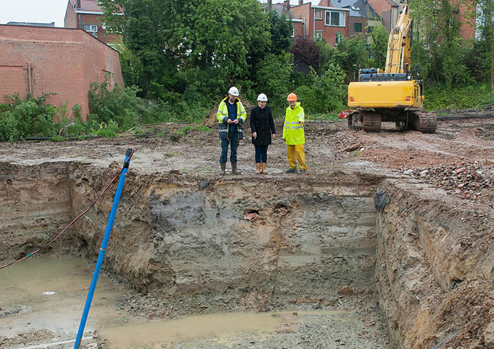 Trois personnes avec des casques de chantier regardent un puits créusé avec une grue en arrière-plan
