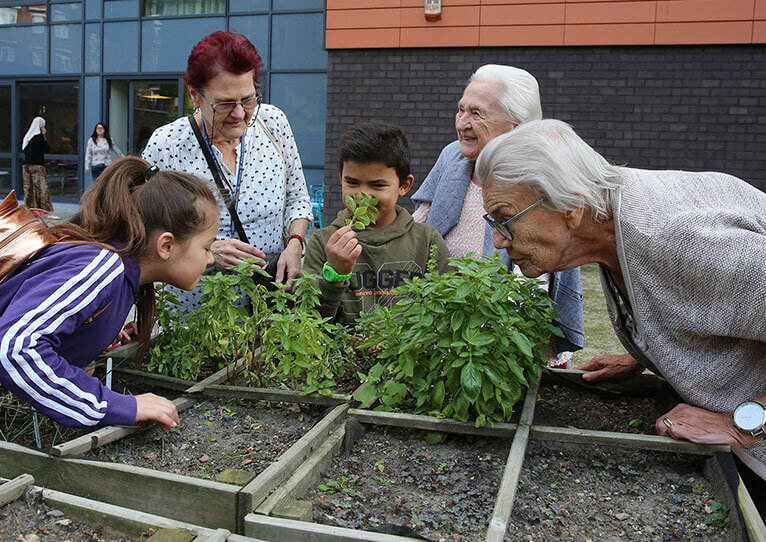 Trois personnes âgées et deux enfants sont rassemblés autour d'un potager dans une maison de repos et sentent les plantes